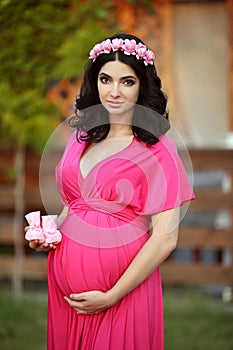 Beautiful pregnant woman holding baby's bootee wearing in pink d