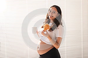 Beautiful pregnant woman holding croissant and cup of coffee in her hands during morning breakfast. Concept of good