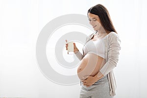 Beautiful pregnant woman holding glass of milk, white background