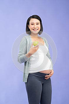 Beautiful pregnant woman holding green apple isolated on lilac