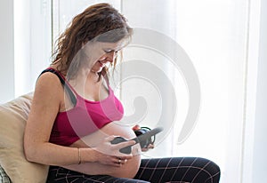 Beautiful pregnant woman holding headphones on her belly for listening music to unborn baby