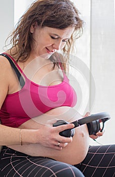Beautiful pregnant woman holding headphones on her belly for listening music to unborn baby