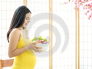 A beautiful pregnant woman in a Japanese room preparing a vegetable salad to eat for good health