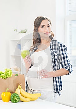 Beautiful pregnant woman in the kitchen with shopping bag and apple