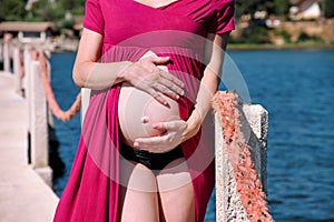 Beautiful pregnant woman and lady is hugging and holding her pregnant belly, standing in natural environment. Waiting for baby.