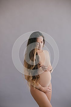 Beautiful pregnant woman with long hair on grey background