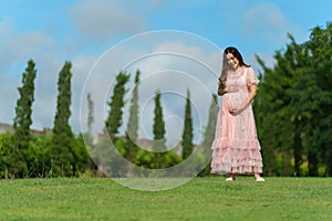 Beautiful pregnant woman looking and stroking her belly in the park