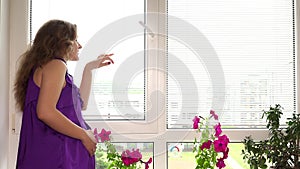 Beautiful pregnant woman looking through window blinds