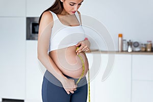 Beautiful pregnant woman measuring her belly with a tape to keep track of her fetus development. Healthy pregnancy concept