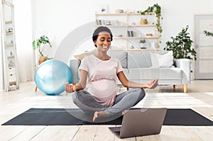 Beautiful pregnant woman meditating to online video on laptop computer at home