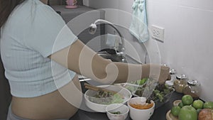 Beautiful pregnant woman preparing fresh vegetable salad in home kitchen.
