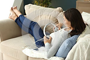 Beautiful pregnant woman putting headphones on belly while resting at home