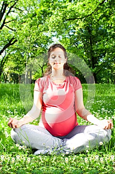 Beautiful pregnant woman relaxing in yoga pose outdoor