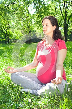 Beautiful pregnant woman relaxing in yoga pose outdoor