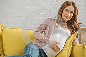 beautiful pregnant woman resting on couch and smiling at camera