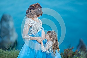 Beautiful Pregnant Woman in romantic flying dress at sea with daughter near ancient ruins of Greece city Gorgeous pregnant girl in