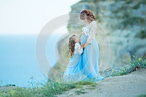 Beautiful Pregnant Woman in romantic flying dress at sea with daughter near ancient ruins of Greece city Gorgeous pregnant girl in