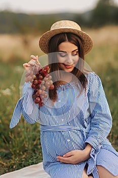 Beautiful pregnant woman show and eat red grapes. Healthy food. Fresh fruits. Happy woman smile