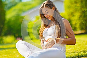 Beautiful pregnant woman sitting outdoor making hand heart gesture on belly