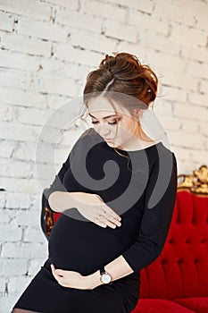 Beautiful pregnant woman sitting on a red sofa. In anticipation