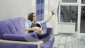 Beautiful pregnant woman sitting on sofa in living room Dalet selfie for social networks. The Internet stream of the