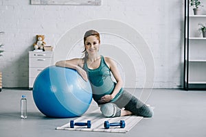 beautiful pregnant woman sitting on yoga mat and leaning on fitness ball