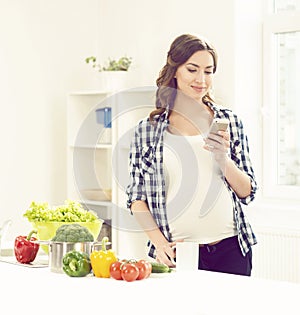 Beautiful pregnant woman with smartphone in kitchen. Motherhood, pregnancy, maternity concept.