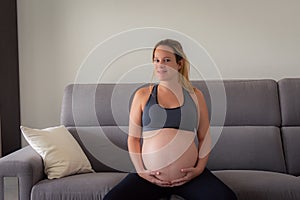 Beautiful pregnant woman in sport clothes sitting at sofa