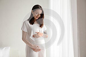 Beautiful pregnant woman standing near window in morning