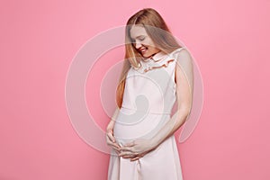 Beautiful pregnant woman stroking her belly on a pink background