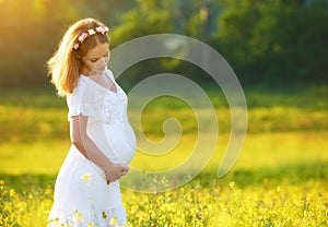 Beautiful pregnant woman in summer nature meadow with yellow flo