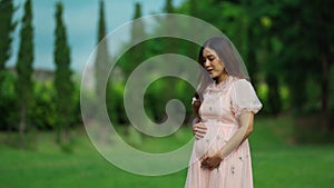 Beautiful pregnant woman talking and stroking her belly in the park