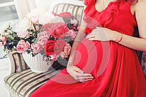 Beautiful pregnant woman touching her belly with hands in the living room