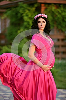 Beautiful pregnant woman touching her belly wearing in pink dres