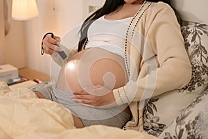 Beautiful pregnant woman using flashlight on belly to stimulate a baby's development, fertility infertility treatment, IVF,