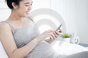 Beautiful pregnant woman using mobile phone in her bedroom.