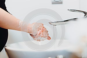 Pregnant woman washing hands and cleaning hands from germs, bacteria and viruses with soap and water