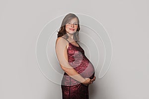 Beautiful pregnant woman wearing red dress standing against grey studio wall background