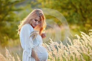 Beautiful pregnant woman in white cotton dress in the summer meadow on a sunset. Concept of pregnancy, maternity, expectation for
