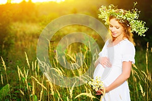 Beautiful pregnant woman in wreath relaxing in summer nature