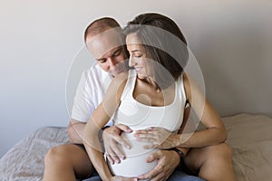 Beautiful pregnant woman and her handsome husband are hugging and smiling while spending time together. Love and couple lifestyle