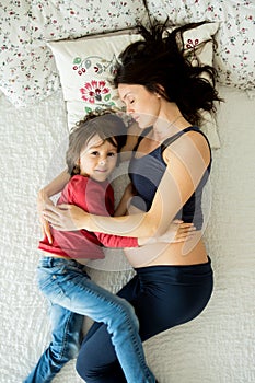 Beautiful pregnant young mother and her child, boy, lie in bed