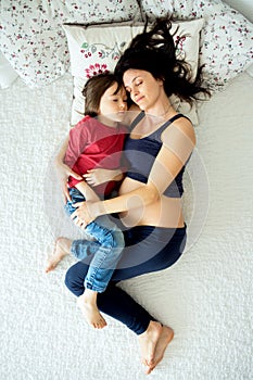 Beautiful pregnant young mother and her child, boy, lying in bed
