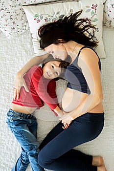 Beautiful pregnant young mother and her child, boy, lying in bed