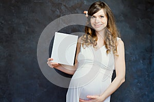 Beautiful pregnant young woman with blank canvas board smiling on black background.