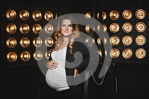 Beautiful pregnant young woman with blond hair and with gentle makeup in the black jacket and in white t-shirt posing