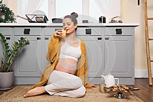 Beautiful pregnant young woman drinking juice in her kitchen