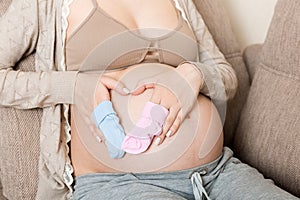 Beautiful pregnant young woman holding a pair of cute baby socks on her tummy, lying on sofa at home