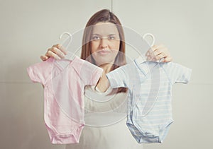 Pregnant woman holding bodysuits for a girl or a boy in soft pa photo
