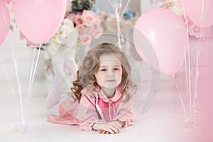 Beautiful preschool girl in a white studio with pink heart-shaped balloons
